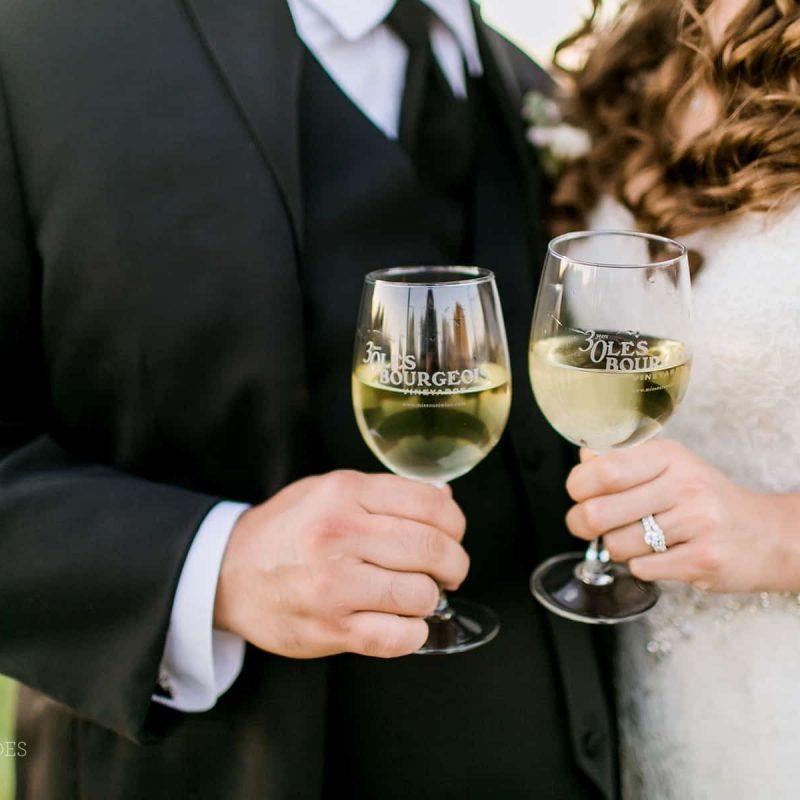 Bride and groom hold Les Bourgeois wine glasses